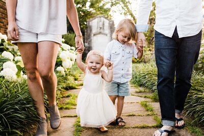 Two adults and two young children, photographed by a family photography Pittsburgh expert, walking hand in hand in a garden.