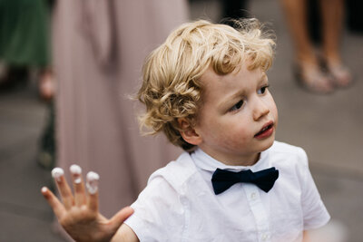 toddler boy with frosting on his fingers from getting an early taste of the wedding cake