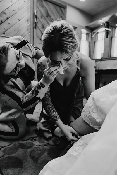 bridesmaid crying, helping the bride put on her wedding shoes
