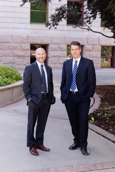 Ramsey Lama and Thom LeDoux stand smiling in suits in downtown Colorado Springs