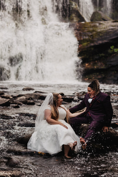 LGBTQ couple sitting on boulders in front of waterfall at their adventure elopement in Tennessee