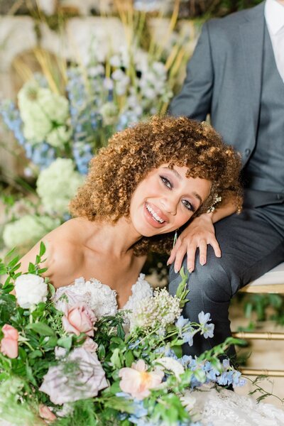 bride smiling while resting on groom's leg in garden wedding