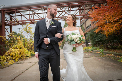 bride and groom walk toward the photographer in front of iron structure and fall colors
