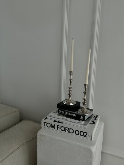 White pedestal with Tom Ford and Peter Lindbergh books, silver candlesticks, and clean interior backdrop