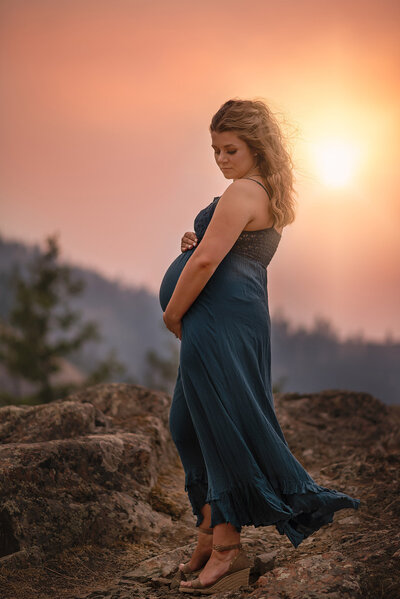 Dramatic portrait of a pregnant women holding her belly with a stunning sunset in the background. Captured in Tobiano by Brittany Danielle Photography.