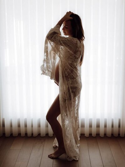 Stijlvolle boudoirfoto van vrouw in kanten kimono voor het raam