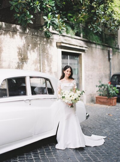 Bride holding her flowers next to the car that will take her to the ceremony with her dad.