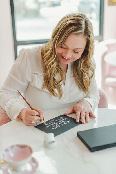 Smiling woman writing white ink calligraphy on black paper