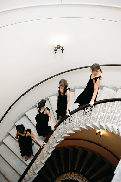 Bridemaids wearing classy black floor length dresses walk down a spiral staircase in Washington DC 