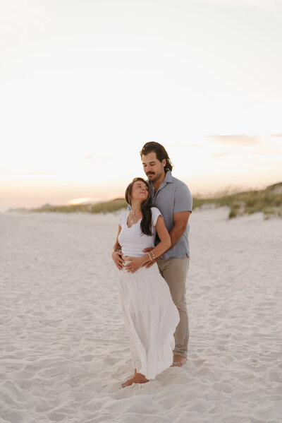 a photo of a man holding his wife from behind during sunset at Grayton Beach, Florida.