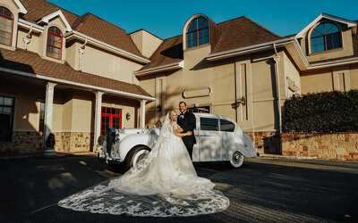 bride and groom posed in front of vintage getaway car
