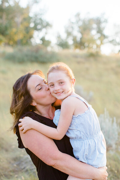 Mom holding little girl and kissing her cheek in a park in Calgary, AB.