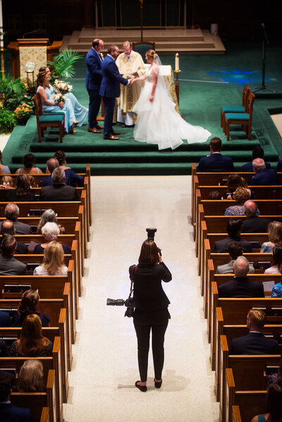A photographer standing in the middle of the aisle taking pictures during a wedding ceremony