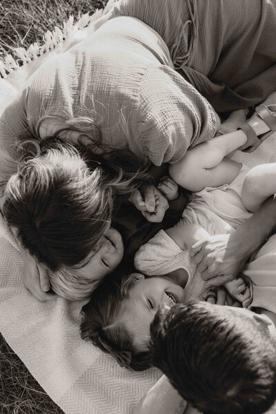 Up-close black and white photo of family laying on blanket in grass.