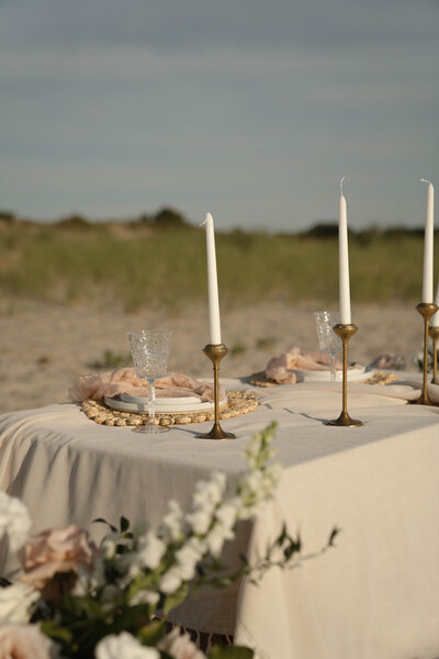 Minimalist beachside tablescape with neutral linens, gold candlesticks, and crystal glassware, styled by Yours Truly, a wedding planner and designer in New Jersey