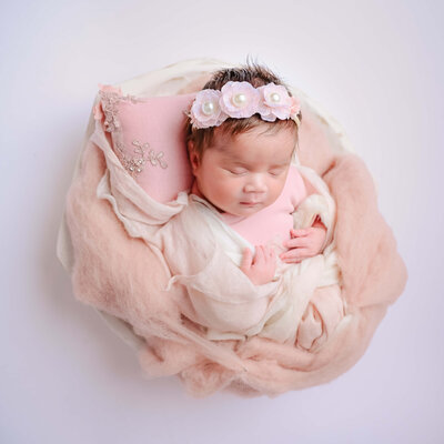 Newborn photo session in Kitsap County, WA. Newborn dressed in pink, wrapped in pink and white fluffs, and posed sleeping in a white bowl. Image captured by Beth Benecki of E. Benecki Photography.