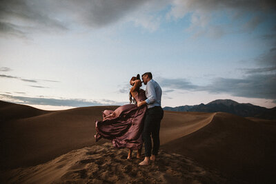 man and woman in pink dress kiss in great sand dunes national park 