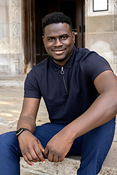 African male wearing dark blue zip up t-shirt and navy blue pants sitting on steps