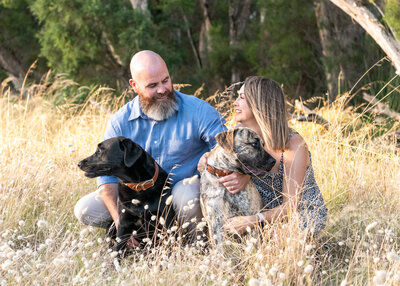 Man and woman kneeling in long grass with their two dogs.