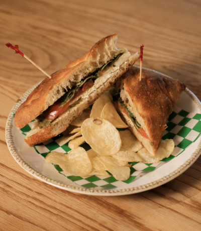 Caprese sandwich with mozzarella, tomato, basil pesto, and greens, served with chips on a plate at Lyla's House in Georgetown, ON.