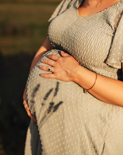 A man and woman stand together with eyes closed and touching foreheads. The woman is pregnant and they're both holding her belly. They're in a snowy field with mountains in the background for maternity pictures.