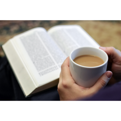 Hands holding a cup of coffee with a bible in the background.