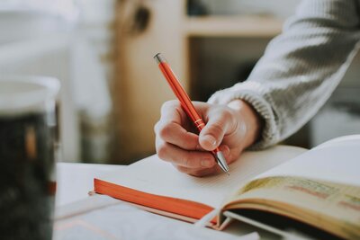 Gros plan sur la main d'un homme qui écrit à la main dans son carnet posé sur son bureau