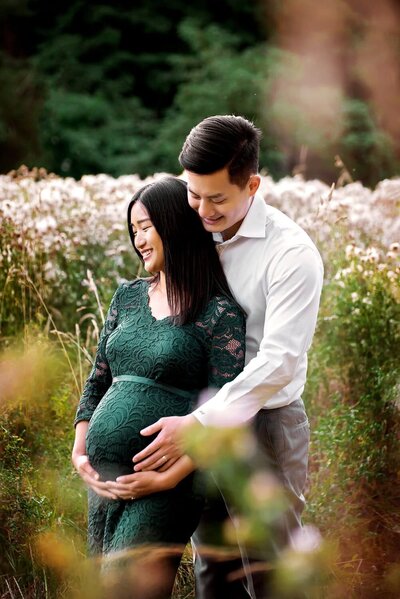 Expecting couple smiling in a field at Deer Lake Park during an outdoor maternity photoshoot in Burnaby.