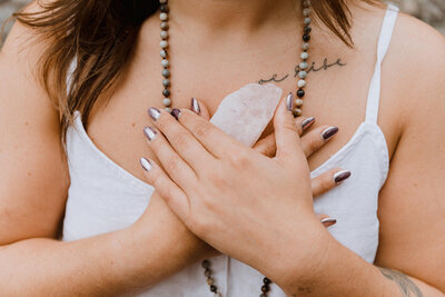 Closeup of woman's hands holding  freeform crystal quartz to her chest