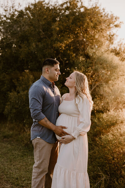 Expecting couple smiling at each other during a gorgeous Georgia sunset.