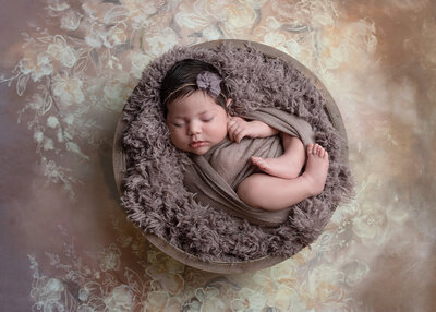 newborn girl wrapped in muted purple in basket with floral background