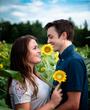 a young dark-haired woman holds a sunflower against her partner's chest and smiles at him