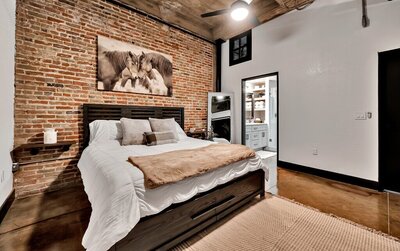 Bedroom with King size bed and exposed brick in this three-bedroom, two-bathroom industrial modern loft condo in the historic Behrens building in downtown Waco, TX.