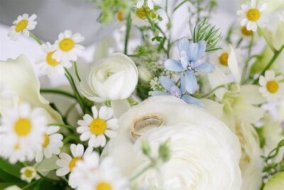 Wedding bands in the middle of a white floral arrangement 