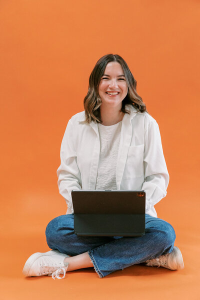 woman in jeans and white shirt smiling and working on laptop