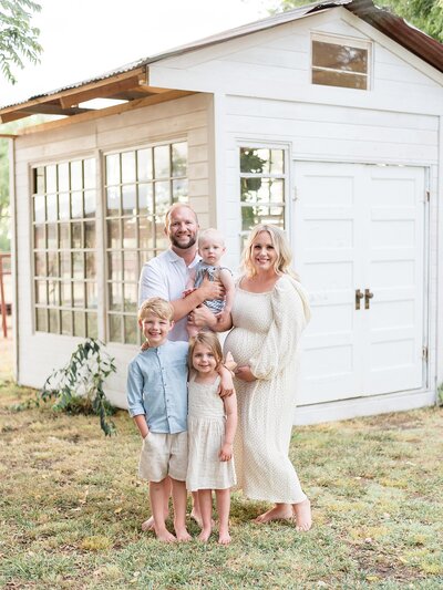 family of five posing in front of green house