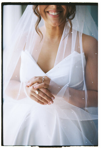 Bride wearing veil and wedding gown smiles into camera, wearing her wedding jewelry