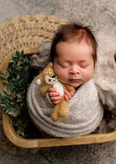 Professional newborn session by Stamford CT photographer featuring baby with knitted teddy bear prop in rustic basket setup