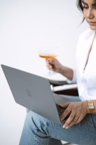Salbine working on a MacBook while enjoying a glass of champagne, blending productivity with a touch of elegance.