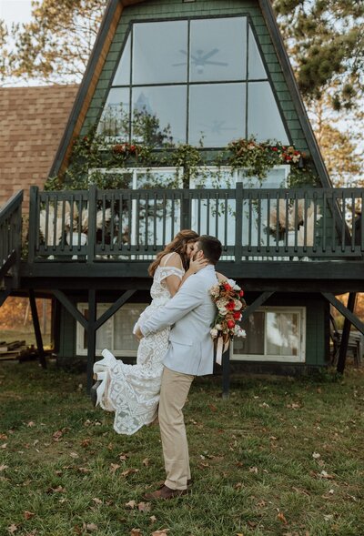 groom lifting bride and kissing in front of an a-frame cabin