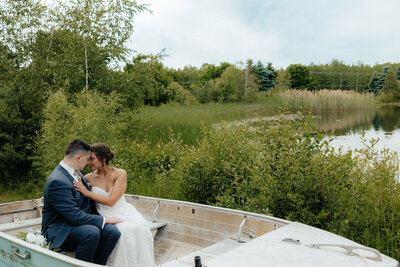 bride and groom sitting in a boat with a pond in the background and green trees