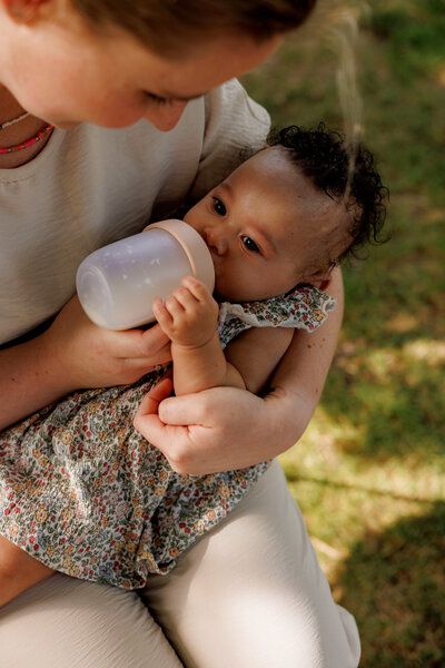 Vrouw voedt een baby met een fles in een rustige, groene omgeving bij Kinderdagverblijf Bij Ons Op De Boerderij.
