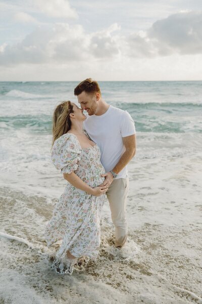 couple laughs on beach during maternity session