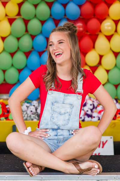 high school senior girl shigh school senior girl sitting  in front of ballon pop game at wayne county ohio fair photographed by Jamie Lynette Photography Canton Ohio Senior Photographer