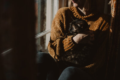 A person holding a black cat as they look out a window