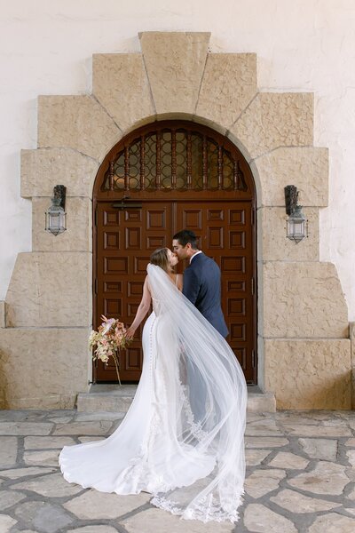 Bride and groom kiss in front of a wooden door during their Santa Barbara Courthouse elopement.