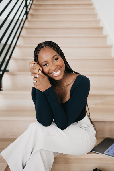Juma Waganda sitting on stairs in a black top and white pants resting her head on her hands