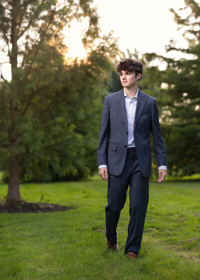 A photo of a casual young man walking in a field at sunset in a suit.