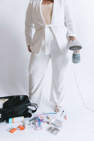 Casey McKenna, founder of Most Valuable Bridesmaid wearing a white suit and holding a steaming garment with a bag of supplies ready to support New York and New Jersey Brides with day-of coordination services.