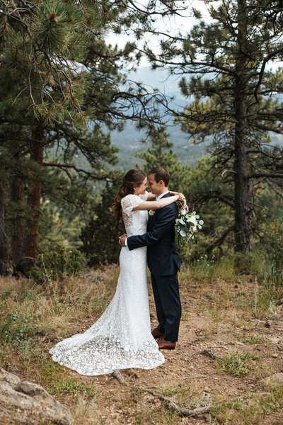 A newlywed couple about to kiss in a wooded area.